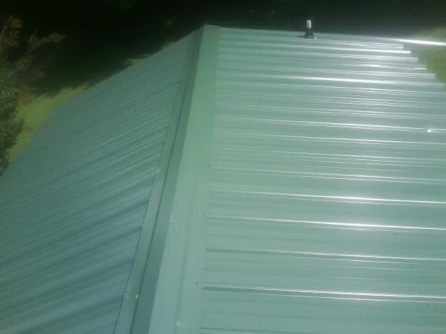 New green metal panels meeting at the ridge of a roof — Flat Roof Repair work by our crew in Falmouth